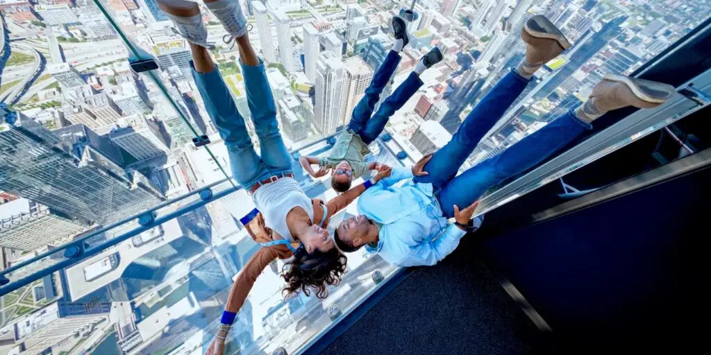 A family lying on The Ledge's glass floor balcony at Skydeck, looking down at the Chicago skyline far below