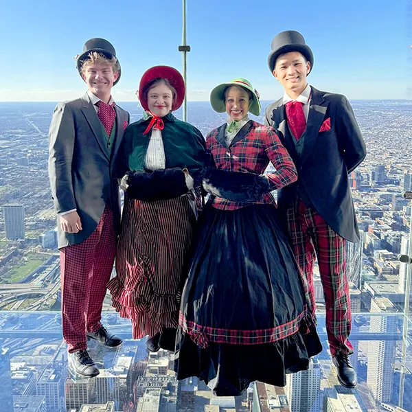 Holiday carolers in Victorian costumes standing on The Ledge at Skydeck Chicago